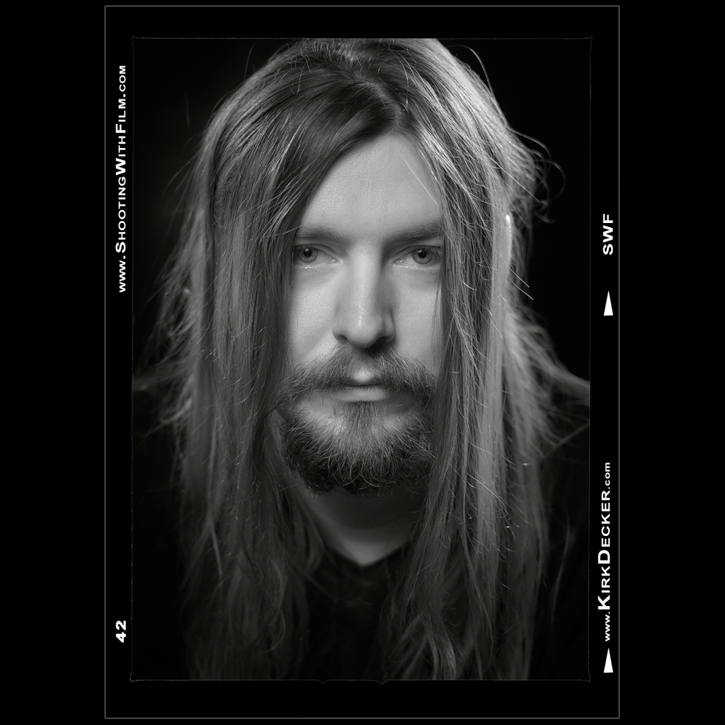 Portrait of artist Ben Parks by Kansas City photographer Kirk Decker.  Ben stares intently into the camera, long hair framing his face.